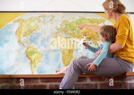 Il ragazzo e la donna matura seduti di fronte Mappa mondo giocando con l'aereo Foto Stock