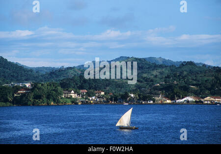 Una piroga vele passato Andoany o Hell-Ville la riva, capitale di Nosy Be Island, dove gli edifici coloniali sono state restaurate, Diana Regione, Madagascar, Oceano Indiano Foto Stock