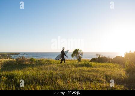 Giovane maschio surfer a piedi con la tavola da surf di sunrise Foto Stock