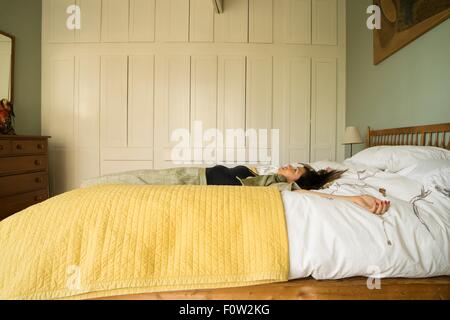 Vista laterale della donna sdraiata sul letto con i bracci aperti Foto Stock