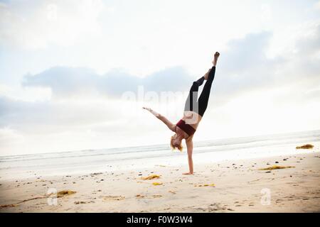 Metà donna adulta a praticare yoga posizione sulla spiaggia Foto Stock