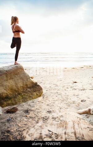 Metà donna adulta struttura pratica yoga pone sulla spiaggia rock Foto Stock