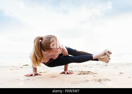 Metà donna adulta in bilico in posizione di yoga sulla spiaggia Foto Stock