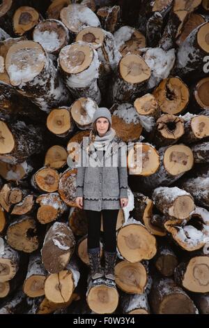 Donna in piedi contro la pila di tronchi in inverno Foto Stock