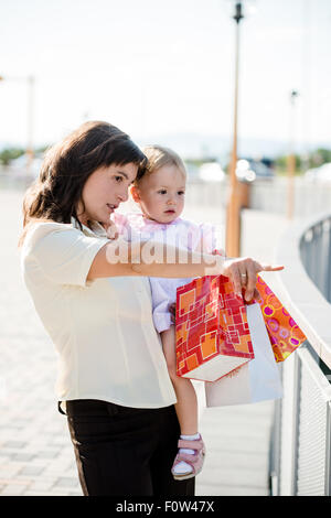 Madre con bambina in abito bianco azienda shopping bags cercando da qualche parte Foto Stock