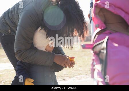 Metà donna adulta Mettere guanti in toddler figlia in posizione di parcheggio Foto Stock