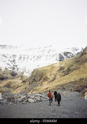 Vista posteriore di tre turisti a piedi verso montagne innevate, Islanda Foto Stock