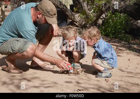 Padre e figli sta tentando di avviare il fuoco di campo utilizzando la lente di ingrandimento e sun, Purros, Kaokoland, Namibia Foto Stock