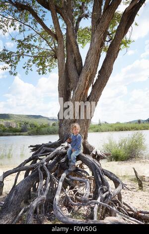 Ragazzo seduto su radici di albero, Ruacana, Owamboland, Namibia Foto Stock