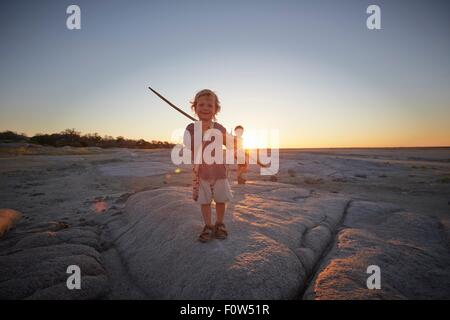 Ritratto di giovane ragazzo in piedi sulla roccia, holding spear, tramonto, Gweta, makgadikgadi, Botswana Foto Stock