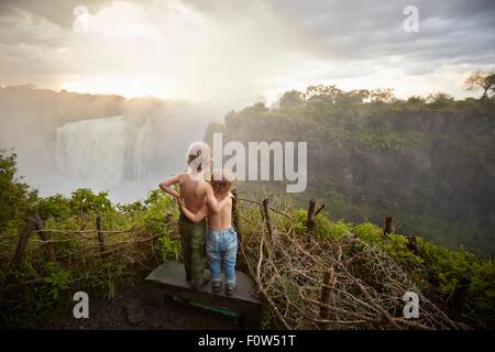 Due giovani ragazzi in piedi sulla mensola ammirando la vista, vista posteriore, Victoria Falls Livingstone, Zimbabwe Foto Stock