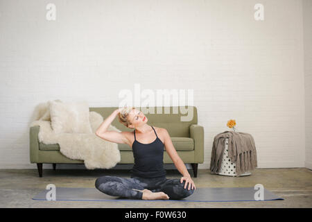 Una donna bionda in un nero leotard e gambali, seduti su un materassino yoga in una camera. Foto Stock