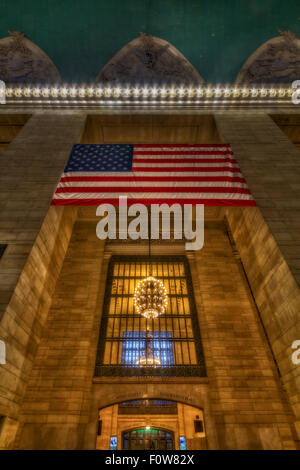 Vista dell'ingresso principale atrio principale al Grand Central Terminal (GCT) nel centro di Manhattan a New York City. Questa vista mostra l'Beaux-Art architettura di stile, come pure la bandiera americana, lampadari e un pezzo di cielo celeste della storica Grand Central Terminal. Il terminale è più di un secolo di vita ed è anche indicata da molti come la Grand Central Station. Foto Stock