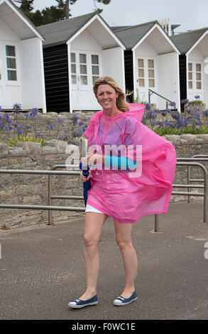 Femmina di vacanzieri con un ombrello e poncho in riva al mare su un umido e ventoso giorno. Bournemouth Inghilterra meridionale REGNO UNITO Foto Stock