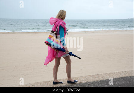 Femmina di vacanzieri con un ombrello e poncho in riva al mare su un umido e ventoso giorno. Bournemouth Inghilterra meridionale REGNO UNITO Foto Stock