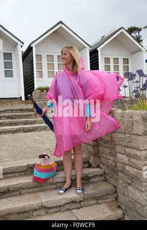 Vacanziere femmina in corrispondenza di un umido località balneare nel Regno Unito vestito in un poncho e tenendo un ombrello Foto Stock