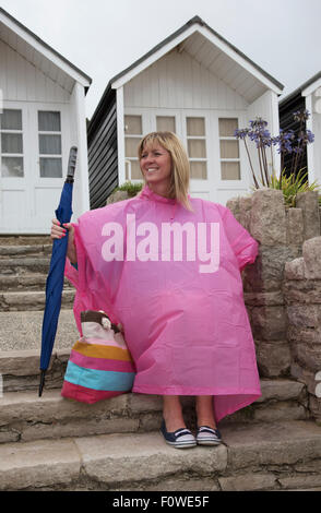 Vacanziere femmina in corrispondenza di un umido località balneare nel Regno Unito vestito in un poncho e tenendo un ombrello Foto Stock