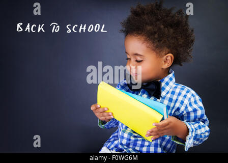 Carino piccolo scolaro ritratto, adorabile bambino africano con libri in mani su sfondo scuro, torna al concetto di scuola Foto Stock