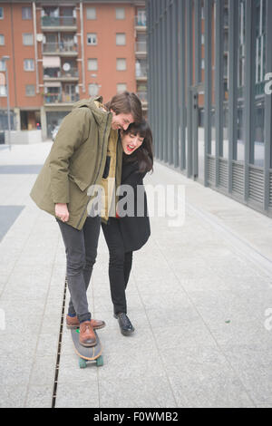 Coppia di bella donna e uomo con i baffi e skate,camminando attraverso le strade della città che abbraccia, giocare e chattare- freschezza, gioventù, concetto carefreeness Foto Stock