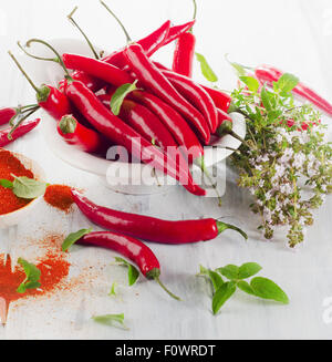Peperoncino rosso con erbe fresche foglie in una ciotola bianco. Messa a fuoco selettiva Foto Stock