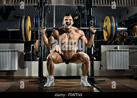 Molto forte guy bodybuilder , eseguire esercizio squatting con peso in palestra Foto Stock