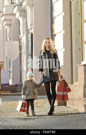 Felice donna e bambino con red shopping bag, camminando sulla strada Foto Stock