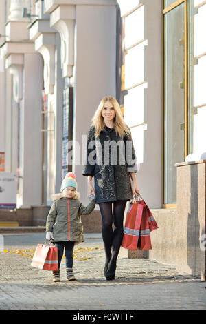 Felice donna e bambino con red shopping bag, camminando sulla strada Foto Stock