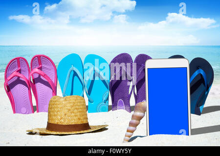 White smartphone con schermo vuoto display, flip flop e un cappello di paglia sulla spiaggia Sunny Beach Foto Stock