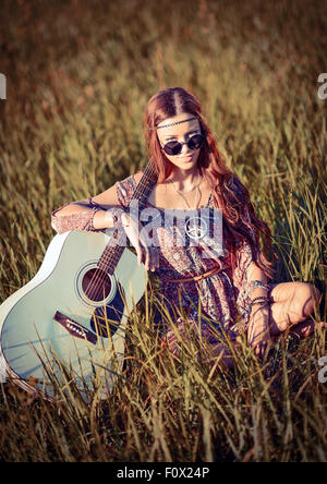 Bella giovane ragazza hippie con la chitarra seduto sull'erba Foto Stock