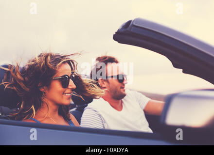 Felice Coppia giovane la guida lungo la strada di campagna nel convertibile al tramonto Foto Stock