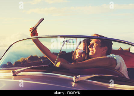 Romantico Coppia Giovane prendendo un Selfie in Classic Vintage Auto sportiva al tramonto Foto Stock