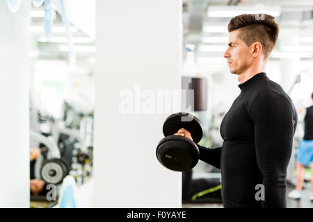 Giovane uomo bello lavorare in una palestra e sollevamento pesi Foto Stock
