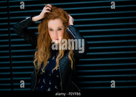 Un giovane attraente redhaired redhead zenzero donna dai capelli modello ragazza in posa con le sue mani in esecuzione attraverso i suoi capelli 3indossando un nero giacca di pelle Foto Stock