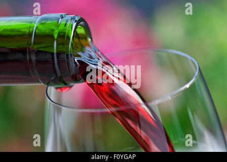 Versare il vino rosso in un bicchiere di vino con fiori da giardino in background Foto Stock