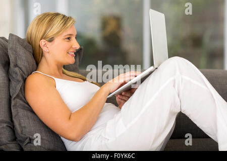 Felice donna incinta sdraiato sul lettino e usando il suo computer portatile Foto Stock