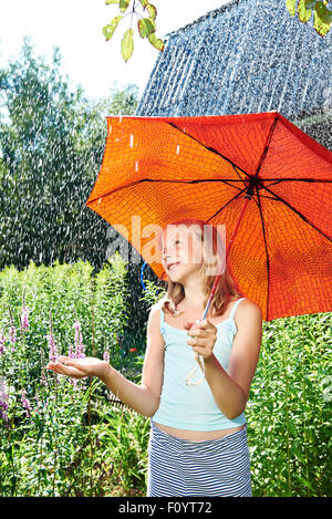 Felice ragazza con ombrello rosso sotto la pioggia di estate Foto Stock