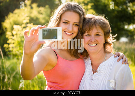 Figlia adolescente e sua madre senior stanno prendendo selfie foto con il telefono cellulare Foto Stock