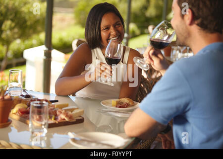 Giovane donna seduta al tavolo con il suo fidanzato di bere vino rosso. Felice coppia giovane a wine bar ristorante. Foto Stock