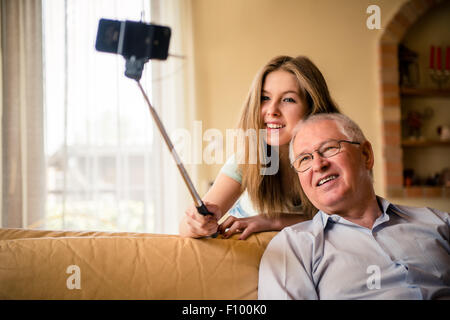 Ragazza adolescente di prendere foto con il telefono cellulare su selfie stick di se stessa e il suo nonno a casa Foto Stock