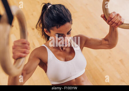 Immagine di forte giovane donna facendo pull-up esercizio utilizzando anelli di ginnastica in palestra. Foto Stock