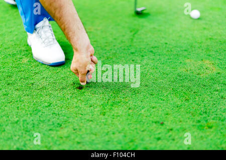 Giocatore di Golf riparazione foro su un verde erba superficie Foto Stock