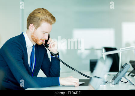 Un bel maschio, dai capelli rossi lavoratore in un call center office a parlare su un telefono cellulare Foto Stock