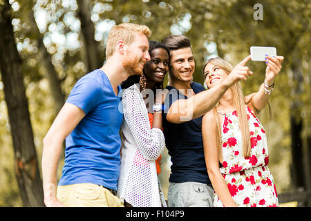 Un gruppo di giovani e coppie tenendo selfies nella natura e sorridente Foto Stock