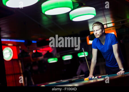 Bel giovane giocatore di snooker la piegatura sopra la tavola in un bar con una bella illuminazione ambientale Foto Stock