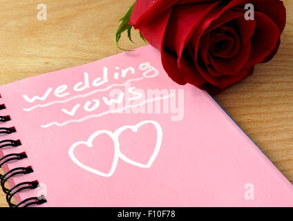 Il blocco note di rosa con i voti di nozze e rose su uno sfondo di legno. Foto Stock