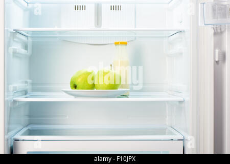 Due mele verdi sulla piastra bianca e una bottiglia di vetro di yogurt in aprire il frigorifero vuoto. Perdita di peso la dieta concetto. Foto Stock