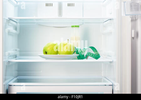 Due mele verdi sulla piastra bianca con nastro di misurazione e una bottiglia di vetro di yogurt in aprire il frigorifero vuoto. Perdita di peso la dieta c Foto Stock