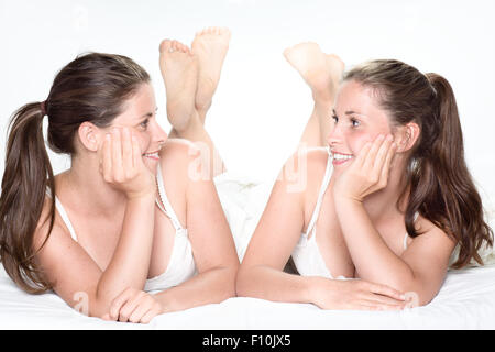 Due sorridente Gemelle posa sul letto guardando ogni altro Foto Stock