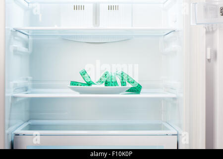 Verde nastro di misurazione sulla piastra bianca in aprire il frigorifero vuoto. Perdita di peso la dieta concetto. Foto Stock