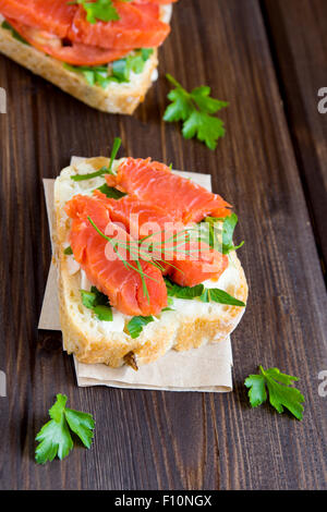 Panino con salmone affumicato (trota), la crema di formaggio, il pomodoro e il prezzemolo rustico sfondo di legno vicino fino Foto Stock